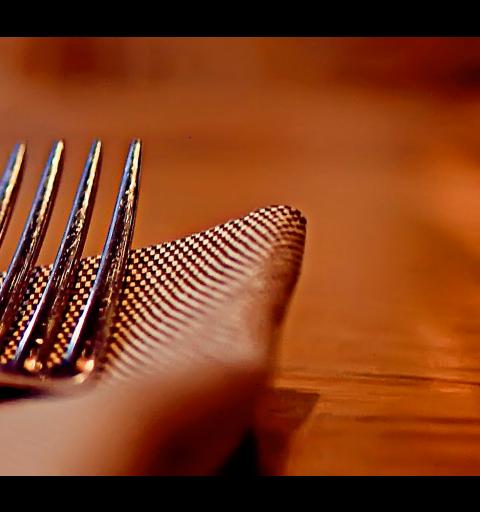 Koristekuva, haarukka ja veitsi lautasliinalla pöydällä.